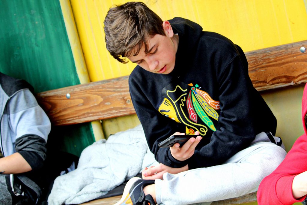 Kille som sitter på sin bänk och tittar på sin mobiltelefon.