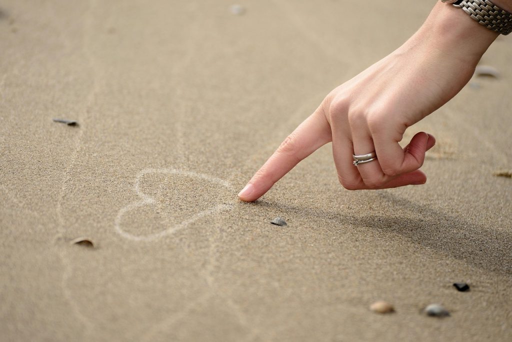 hand som ritar ett hjärta i sanden